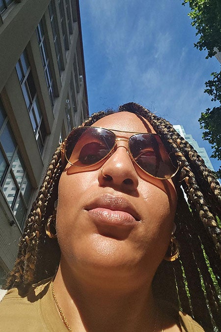 Selfie of the author looking at her phone while walking down a city street wearing sunglasses and a gold blouse.